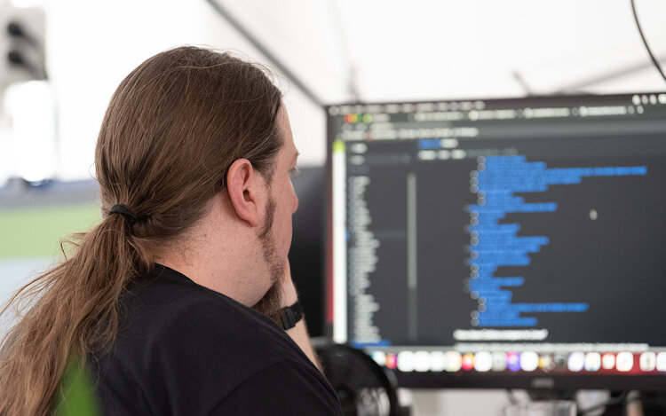 Mann mit Zopf sitzt vor einem Bildschirm und programmiert etwas