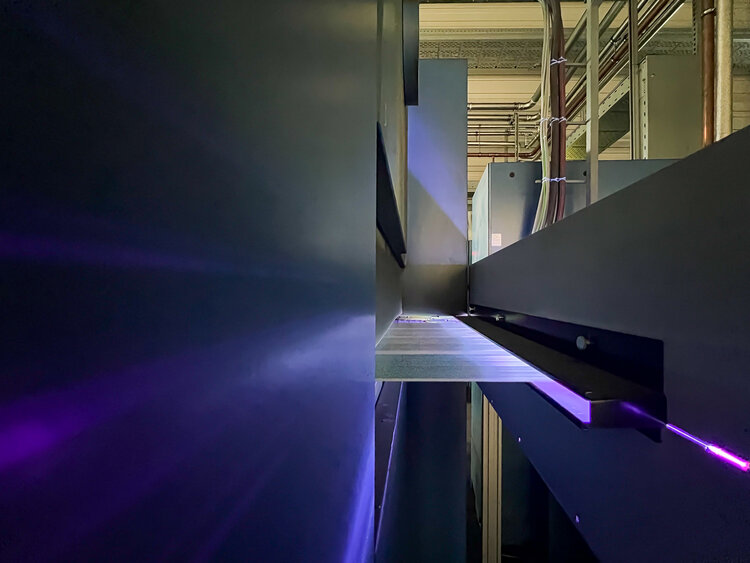 Blau-lila leuchtend sieht man die Papierbahn aus der LED-Trockeneinheit in den ausgeschalteten Trockner der Rollenoffsetmaschine einlaufen.
