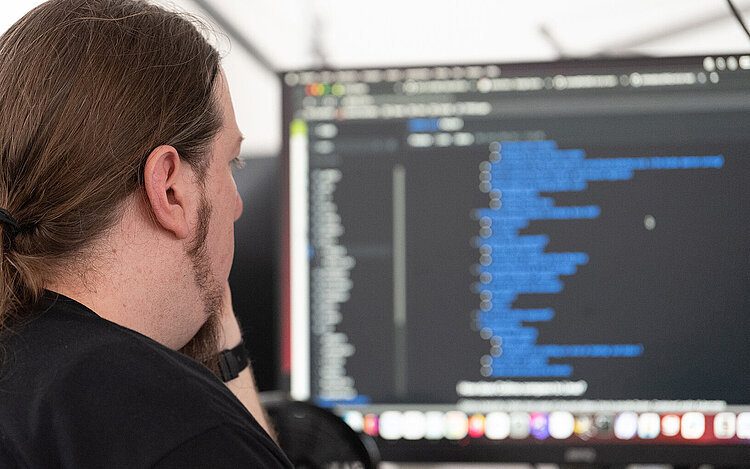 Mann sitzt vor einem Bildschirm und programmiert etwas