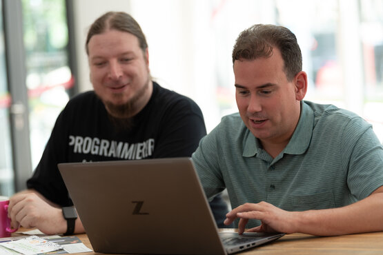 2 Männer sitzen zusammen vor einem Laptop