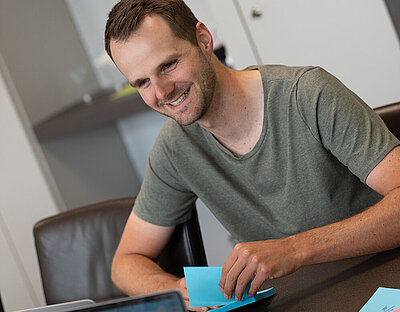 Mann sitzt lächelnd an Konferenztisch mit bunten Kärtchen