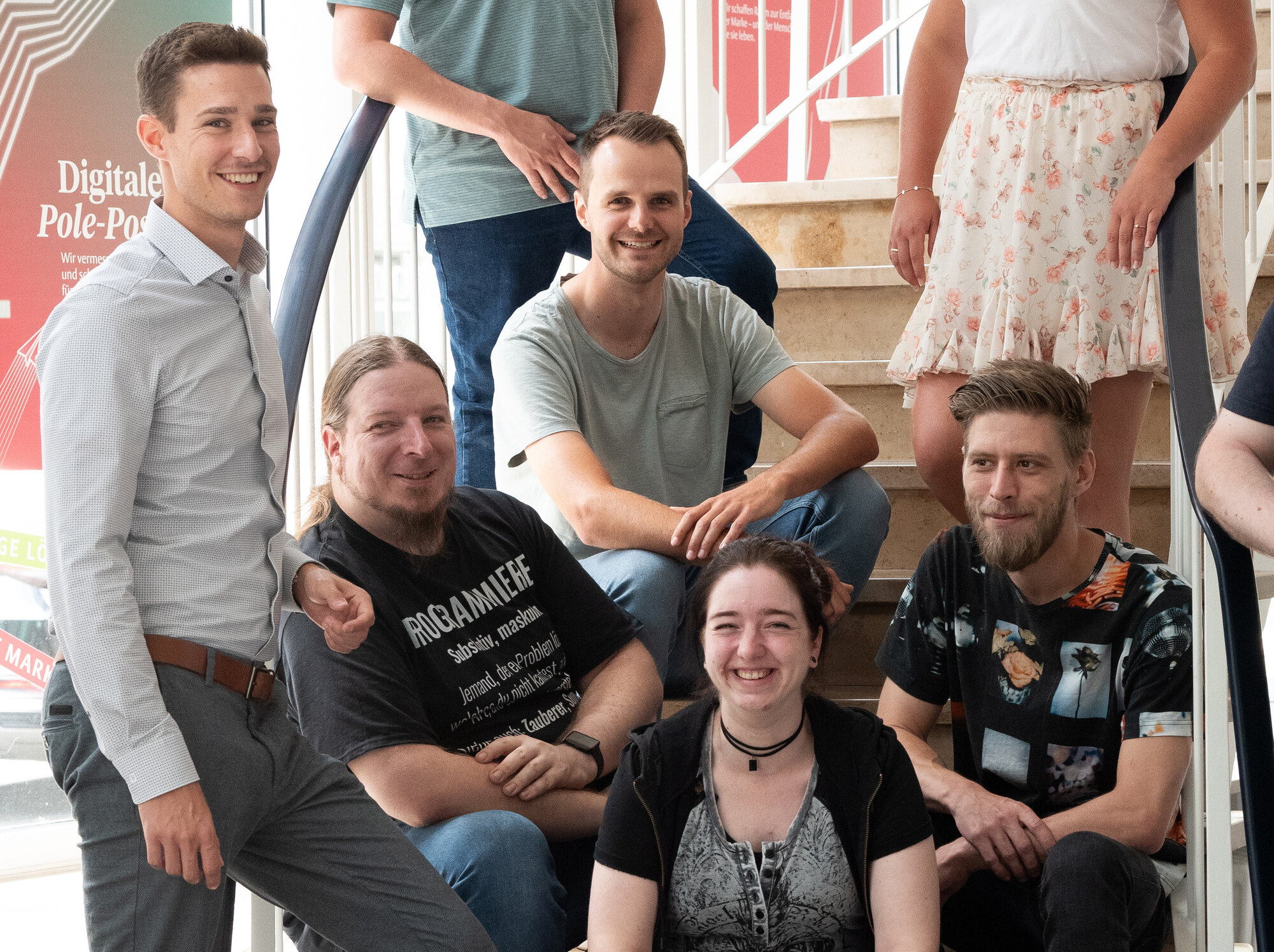 Gruppe von Menschen auf Treppe angeordnet lachen fröhlich in die Kamera