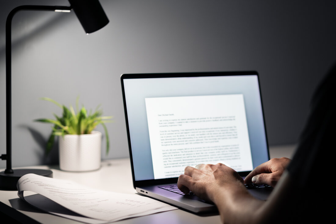Person sitzt vor aufgeklapptem Laptop und schreibt etwas in einem Textprogramm