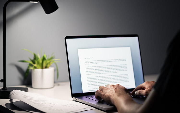 Text schreiben Person sitzt vor aufgeklapptem Laptop und schreibt etwas in einem Textprogramm