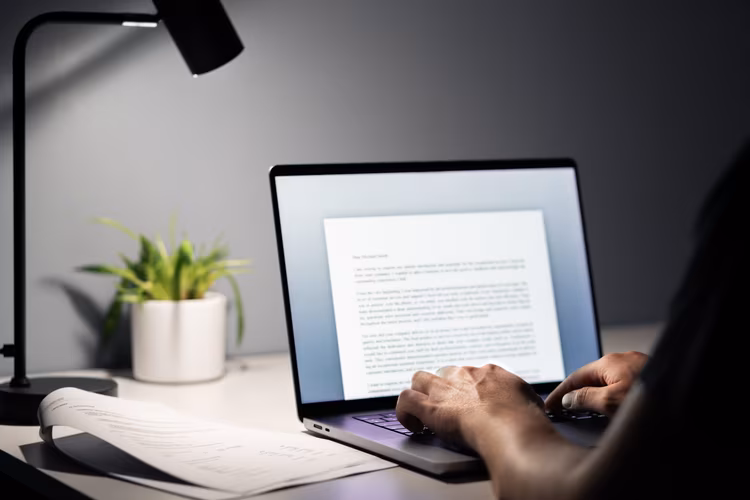 Text schreiben Person sitzt vor aufgeklapptem Laptop und schreibt etwas in einem Textprogramm