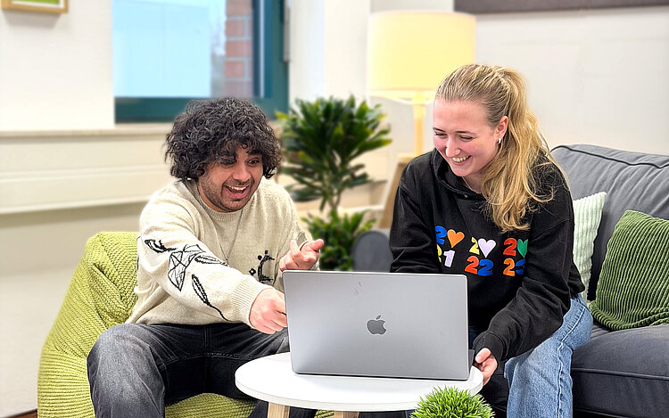 Zwei Kollegen schauen zusammen auf einen Bildschirm und sind begeistert.