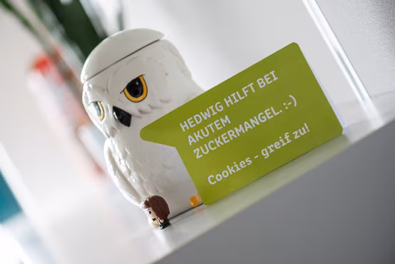 Eine weiße Keksdose in Form einer Eule und ein grünes Schild, dass dazu einlädt, sich Kekse zu nehmen