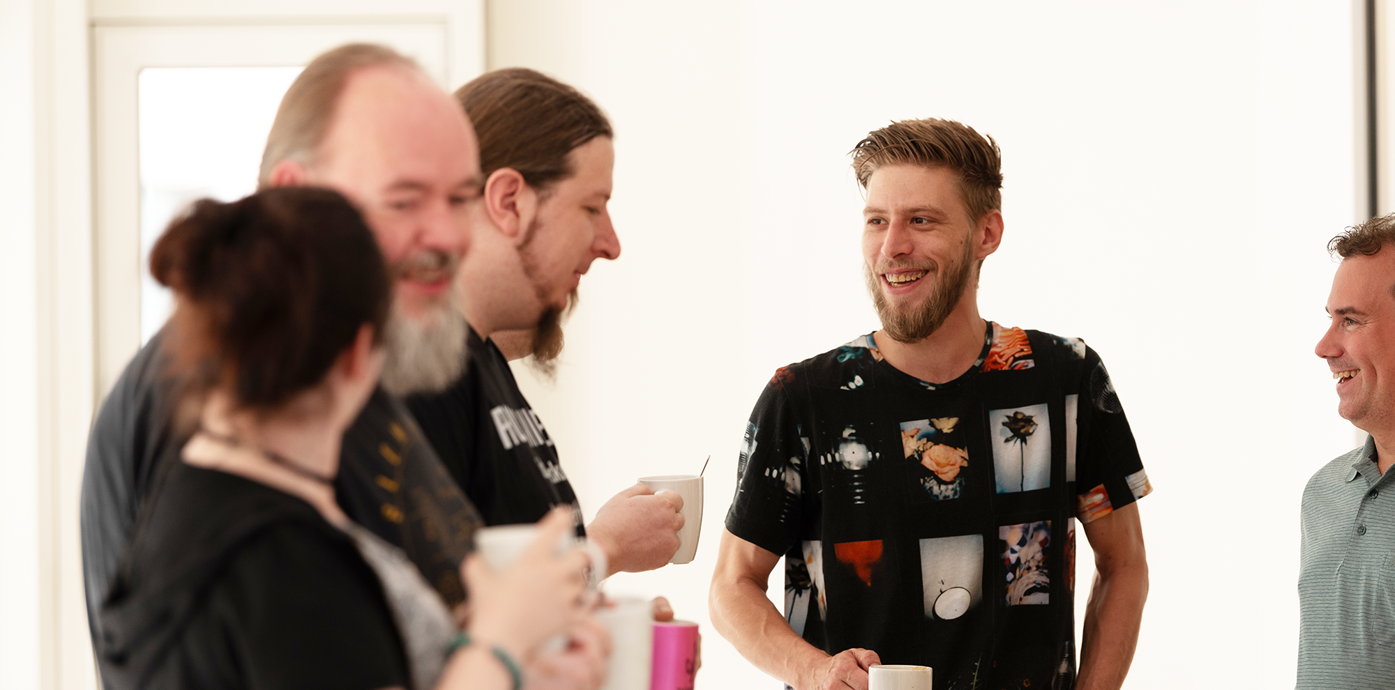 Eine Gruppe aus 5 Personen unterhalten sich fröhlich mit einer Tasse in der Hand