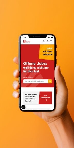 Vor einem orangenen Hintergrund hält eine Hand ein iPhone auf dem die mobile Webseite von Caritas Soest dargestellt wird