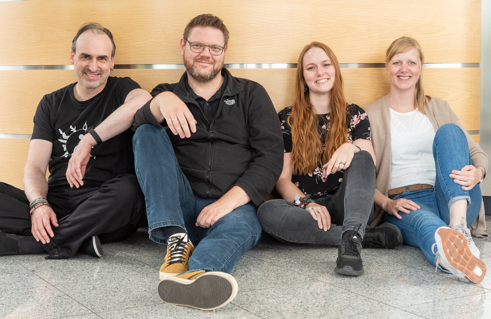 2 Männer und 2 Frauen sitzen nebeneinander auf dem Boden und lächeln in die Kamera