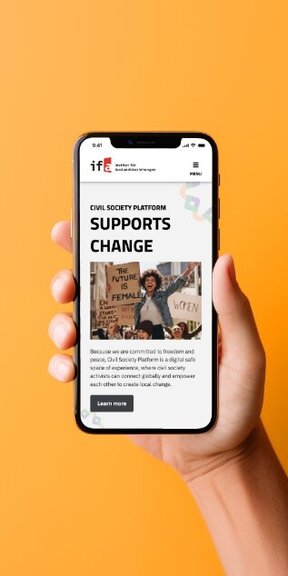 Vor einem farbigen Hintergrund hält eine Hand ein iPhone auf dem die mobile Webseite Civil Society Platform der IFA Germany dargestellt wird