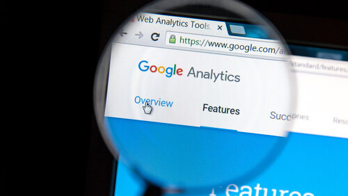 Lupe, die über einen Computer gehlaten wird, der google analytics anzeigt