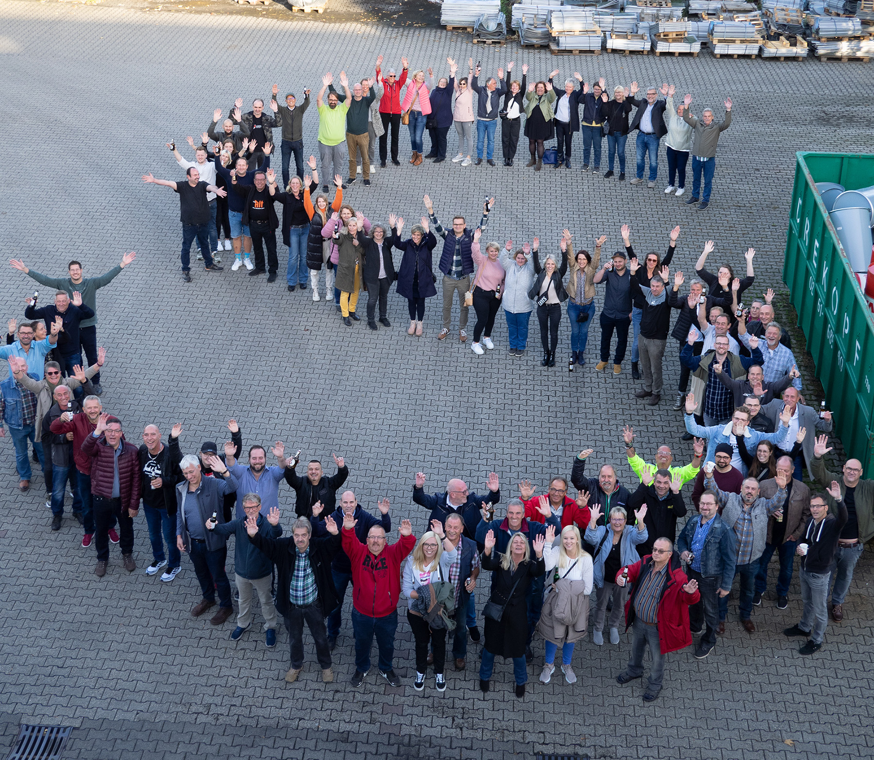 Mitarbeiter von Schaffrath bilden ein S auf dem Außengelände, Foto von oben.