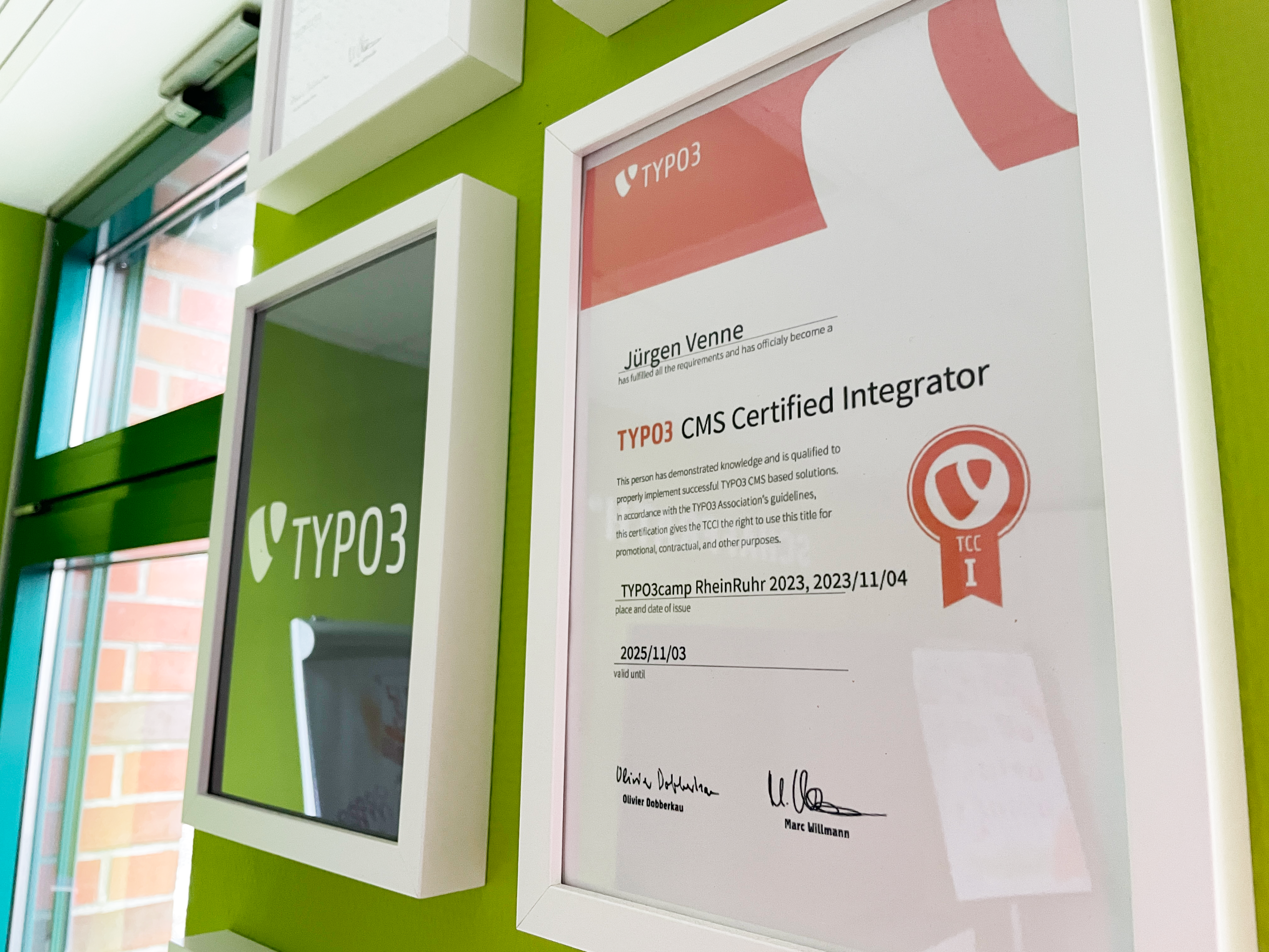 TYPO3 Zertifikat im weißen Bilderrahmen an grüner Wand in schrägem Winkel aufgenommen