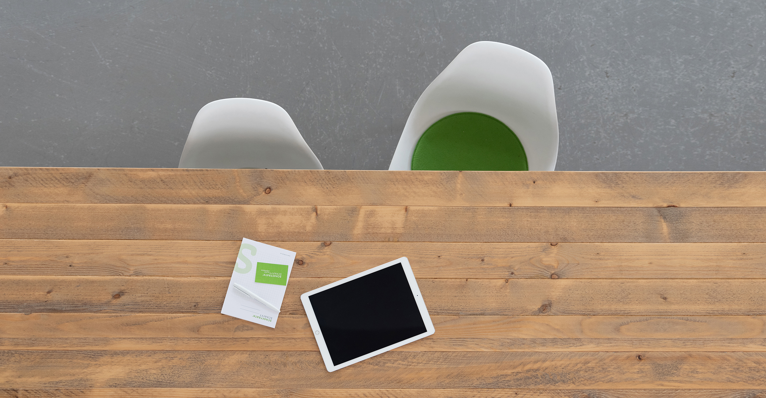 Tisch von oben mit 2 Stühlen davor. Auf dem Tisch liegt ein Block und ein Tablet