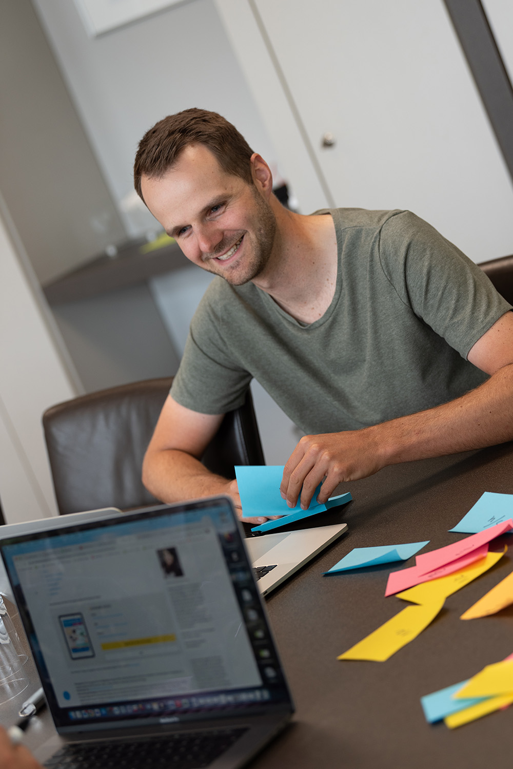 Mann sitzt lächelnd an Konferenztisch mit bunten Kärtchen