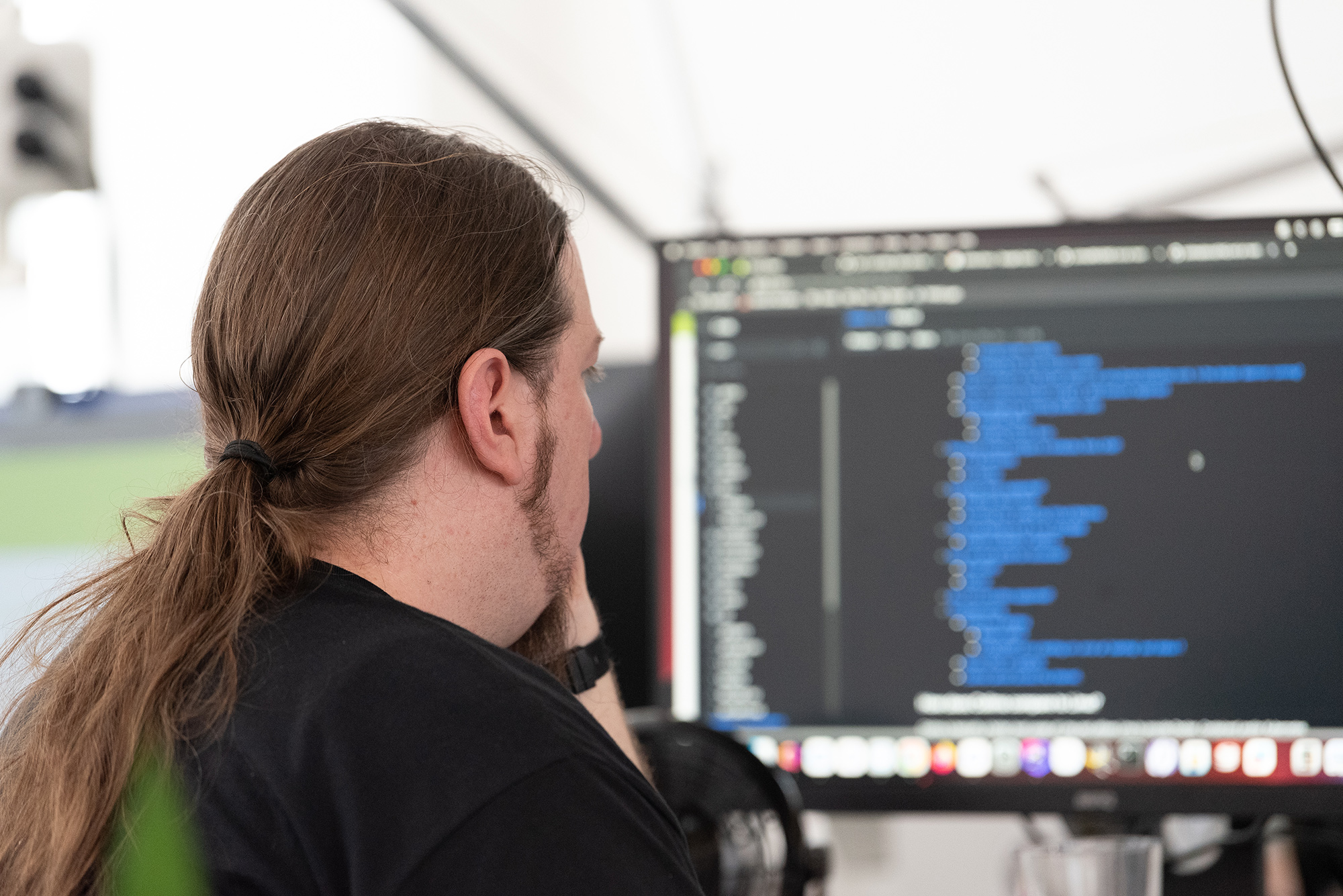 Coding Mann mit Zopf sitzt vor einem Bildschirm und programmiert etwas