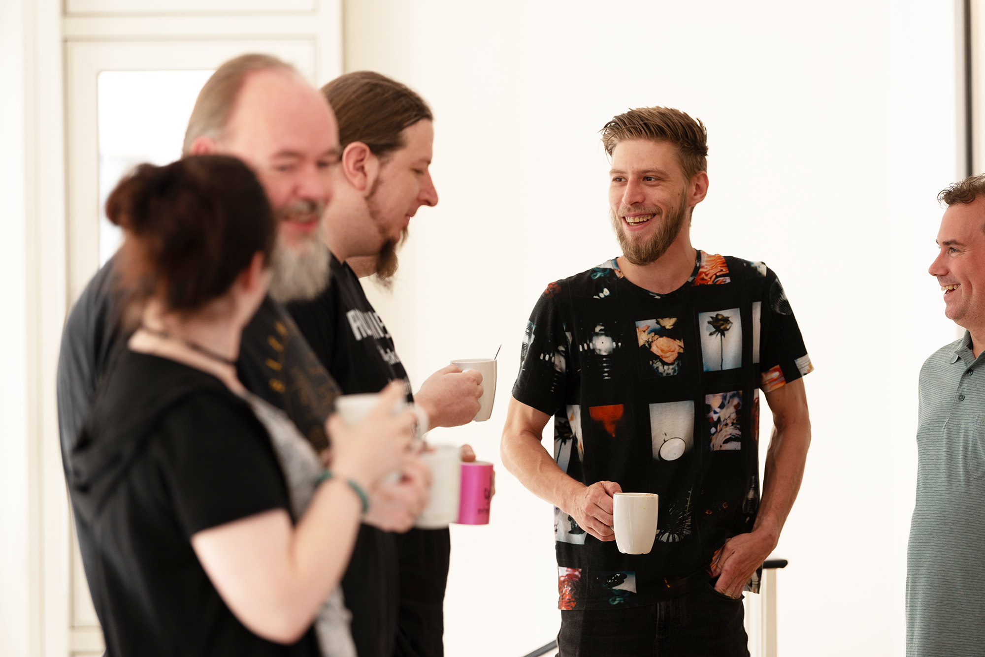Eine Gruppe aus 5 Personen unterhalten sich fröhlich mit einer Tasse in der Hand